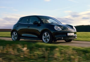 Schwarzer GWM ORA 03 fährt bei Sonnenuntergang über eine schmale Landstraße; im Hintergrund Felder und ein bewölkter Himmel.