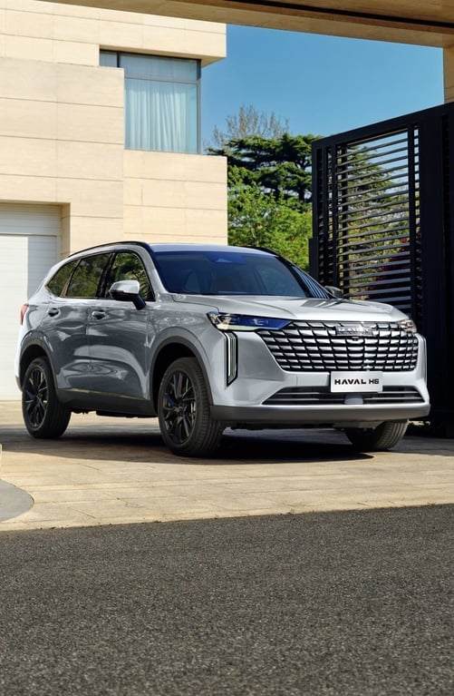 Silbergrauer GWM HAVAL H6 vor einem modernen Haus mit offenem Einfahrtstor an einem sonnigen Tag.