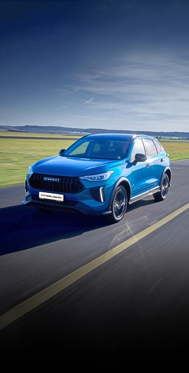 Blauer GWM Haval Jolion Pro SUV fährt auf einer Landstraße durch eine grüne, leicht hügelige Landschaft unter klarem blauem Himmel.
